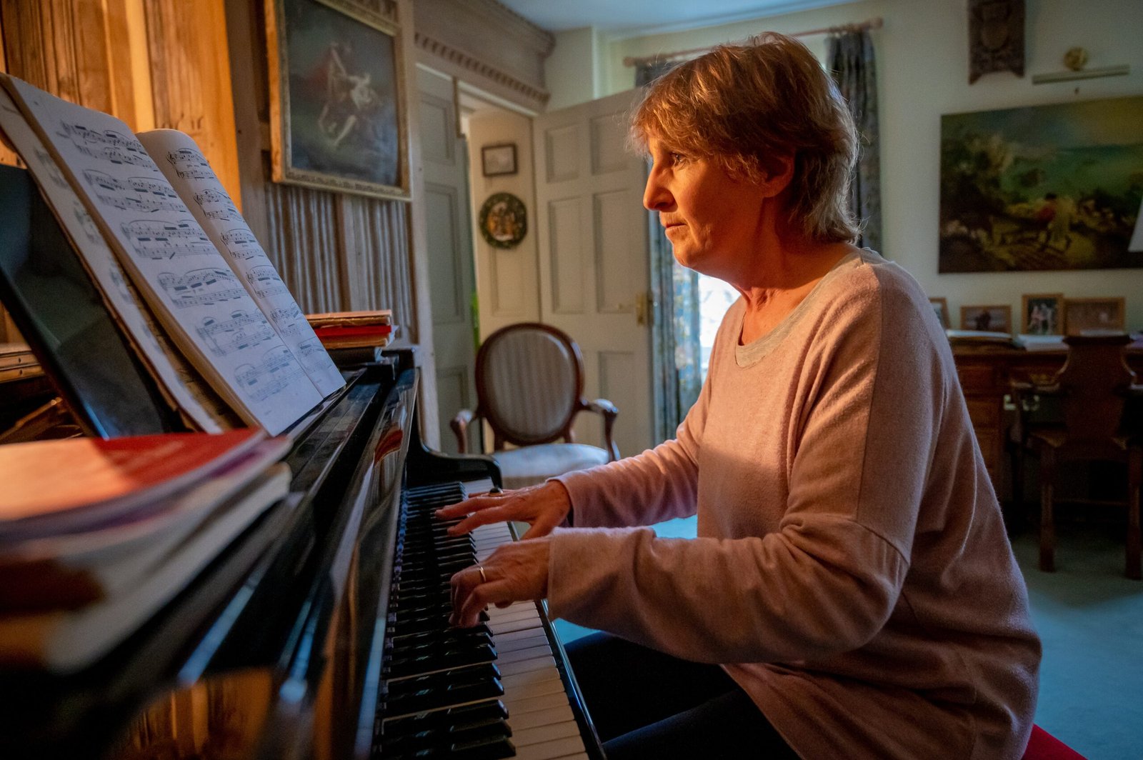 Mulher idosa tocando piano em casa enquanto lê uma partitura