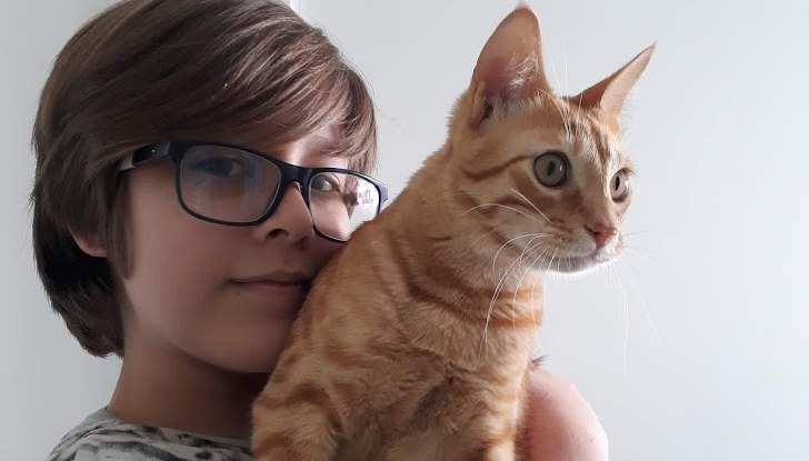 Criança de óculos segurando no colo um gato laranja