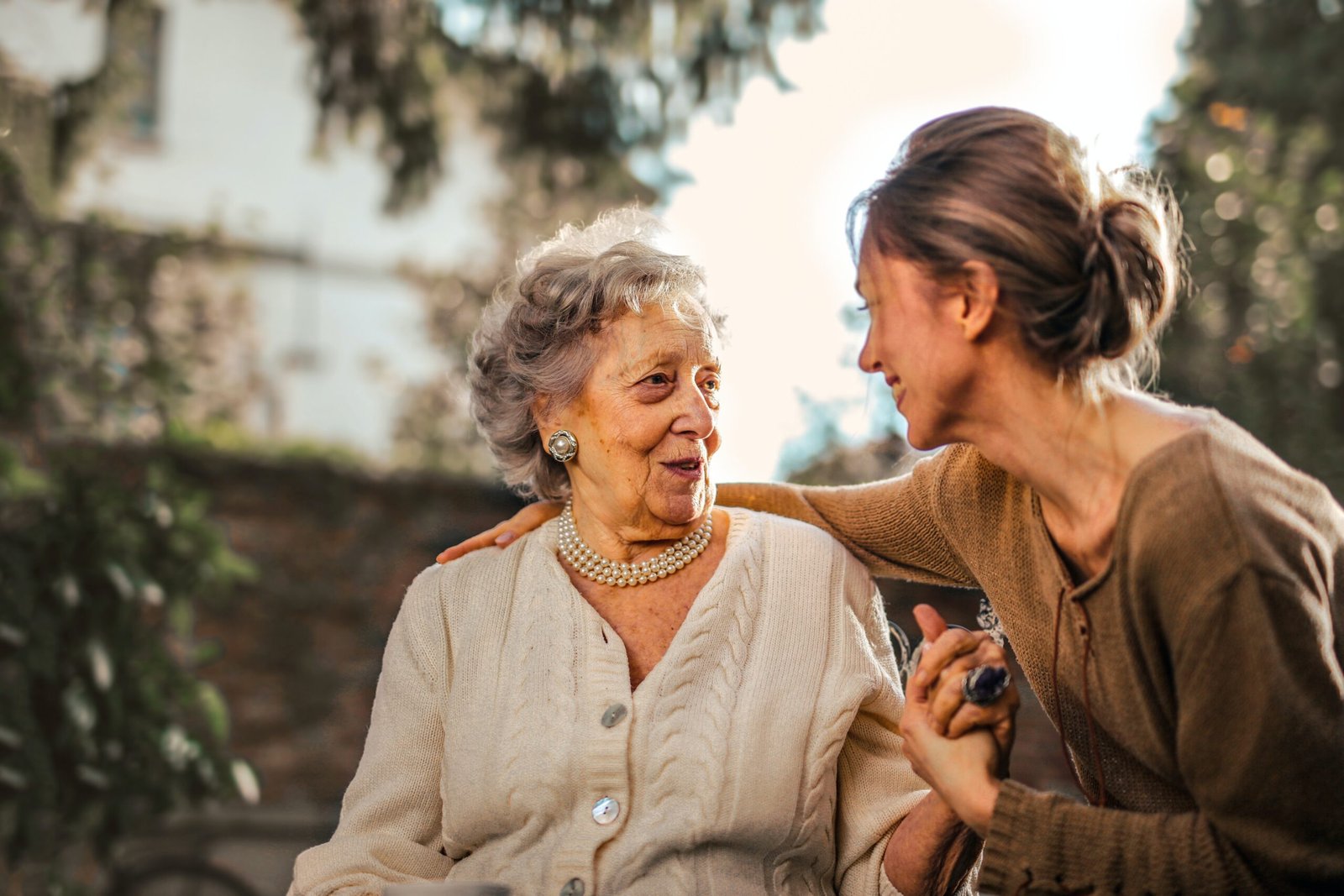 Mulher idosa e uma mulher mais jovem de mãos dadas, conversando e sorrindo ao ar livre